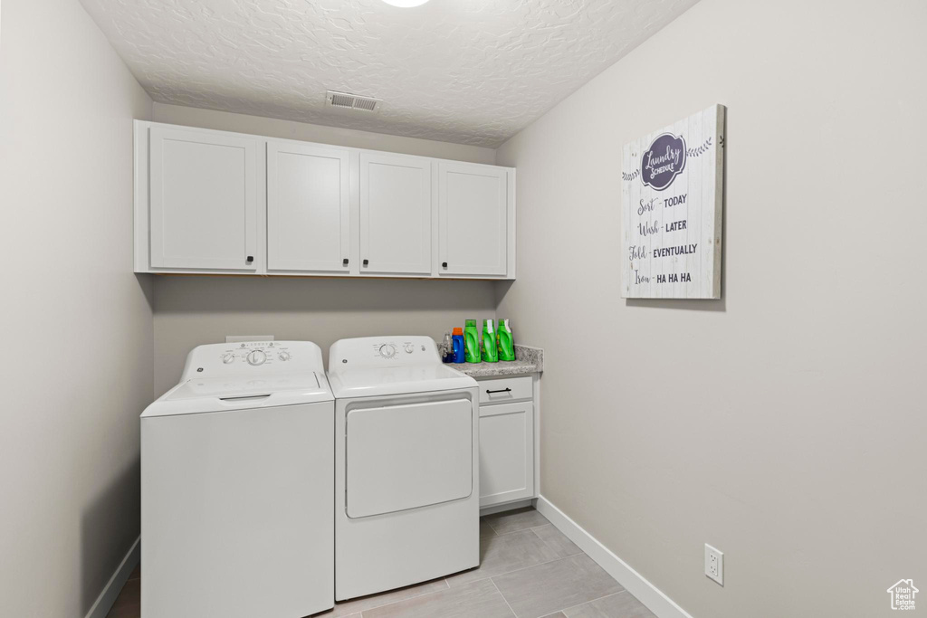 Clothes washing area with visible vents, independent washer and dryer, a textured ceiling, cabinet space, and baseboards