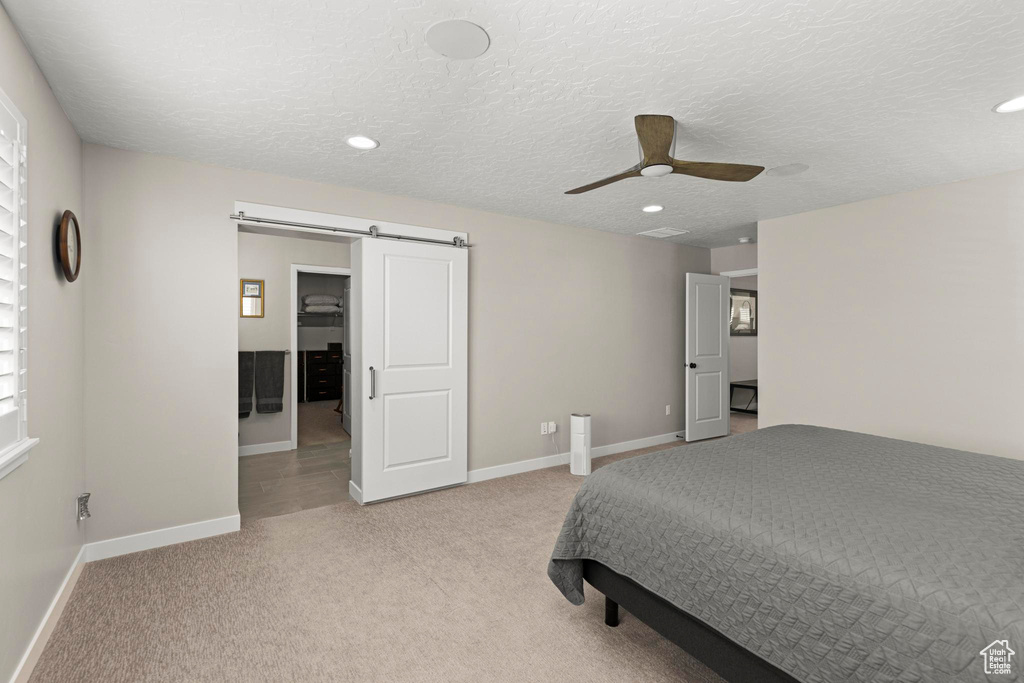 Bedroom featuring a textured ceiling, a barn door, baseboards, light colored carpet, and ceiling fan