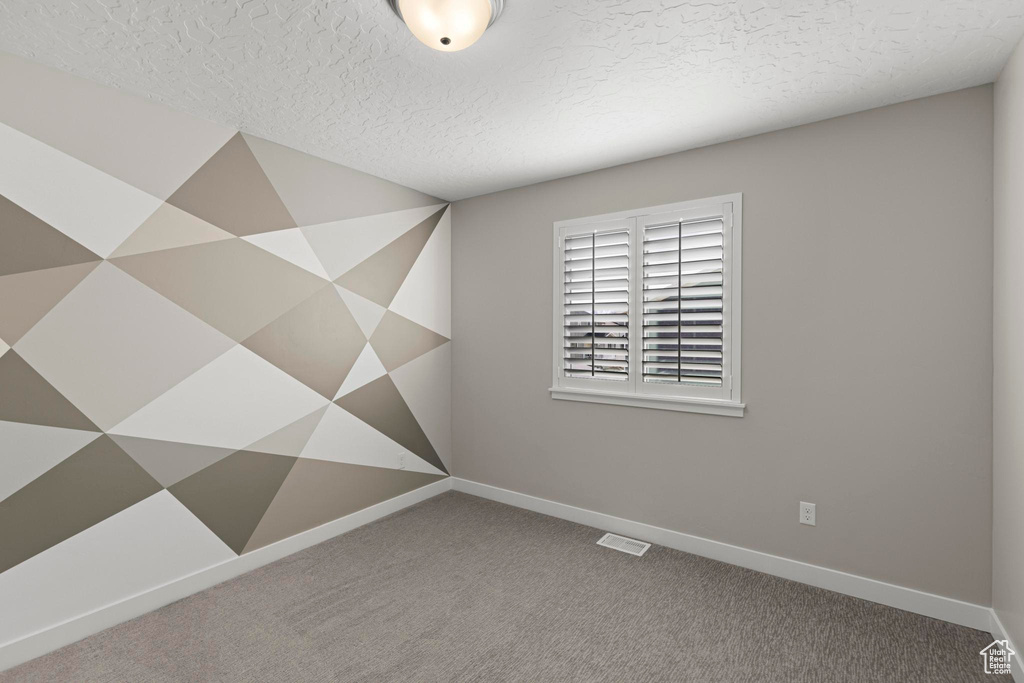 Carpeted empty room with visible vents, a textured ceiling, and baseboards