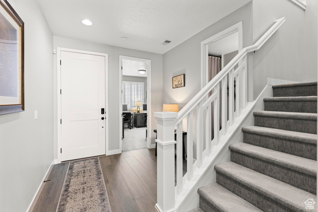 Entrance foyer featuring dark wood-style floors, visible vents, baseboards, recessed lighting, and stairs