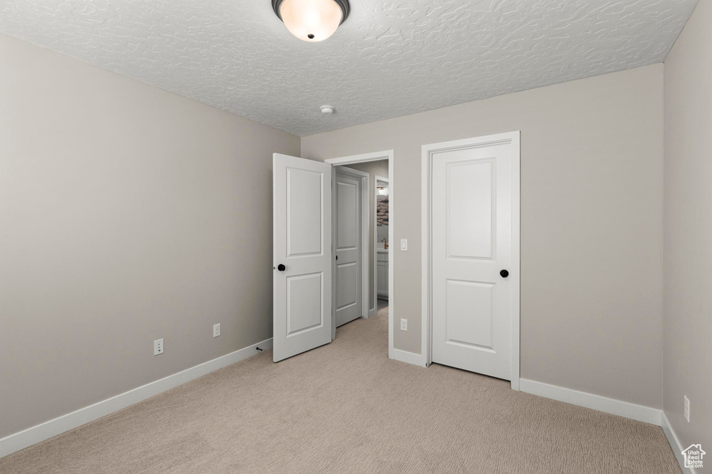 Unfurnished bedroom with light carpet, a textured ceiling, and baseboards