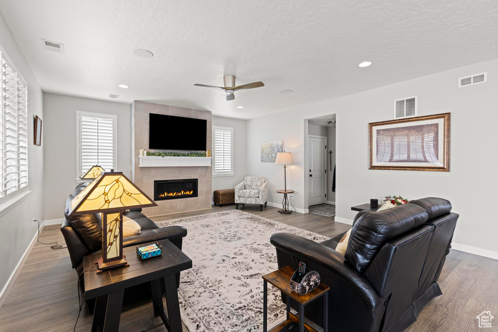 Living area featuring a ceiling fan, baseboards, wood finished floors, visible vents, and a tile fireplace