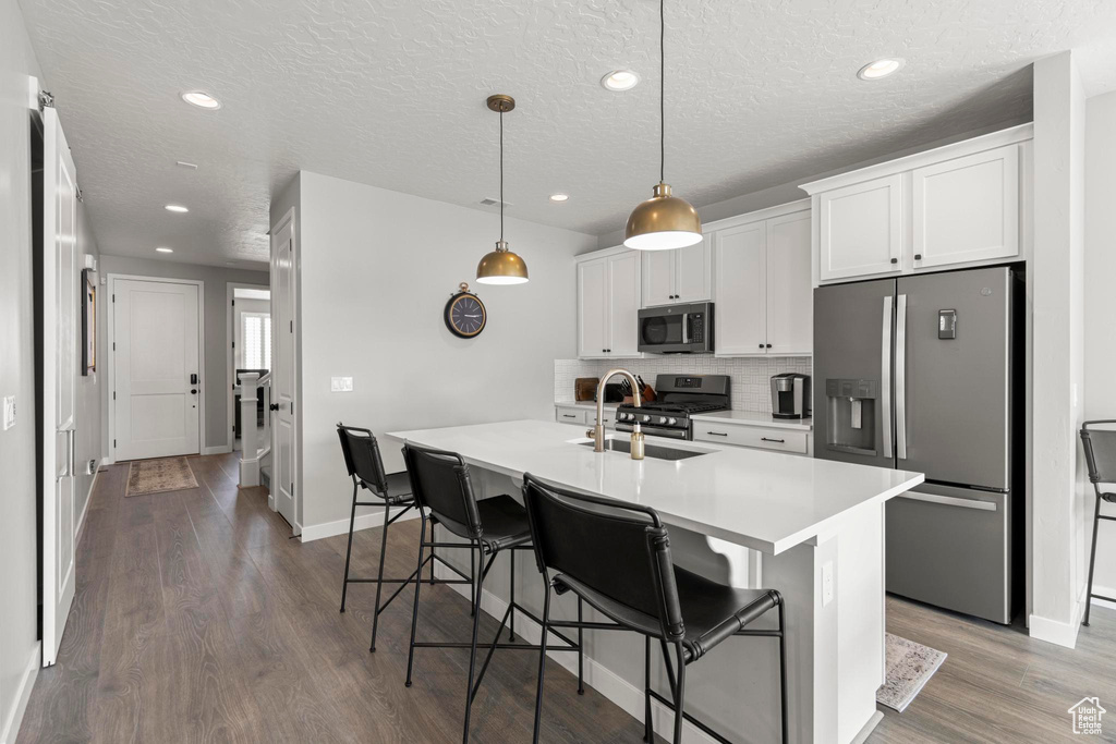 Kitchen with wood finished floors, a center island with sink, a sink, stainless steel appliances, and a kitchen bar