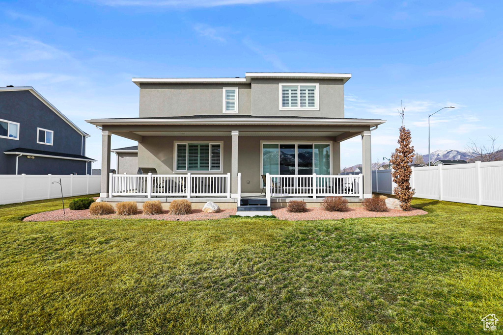 Back of house with stucco siding, a lawn, covered porch, and fence