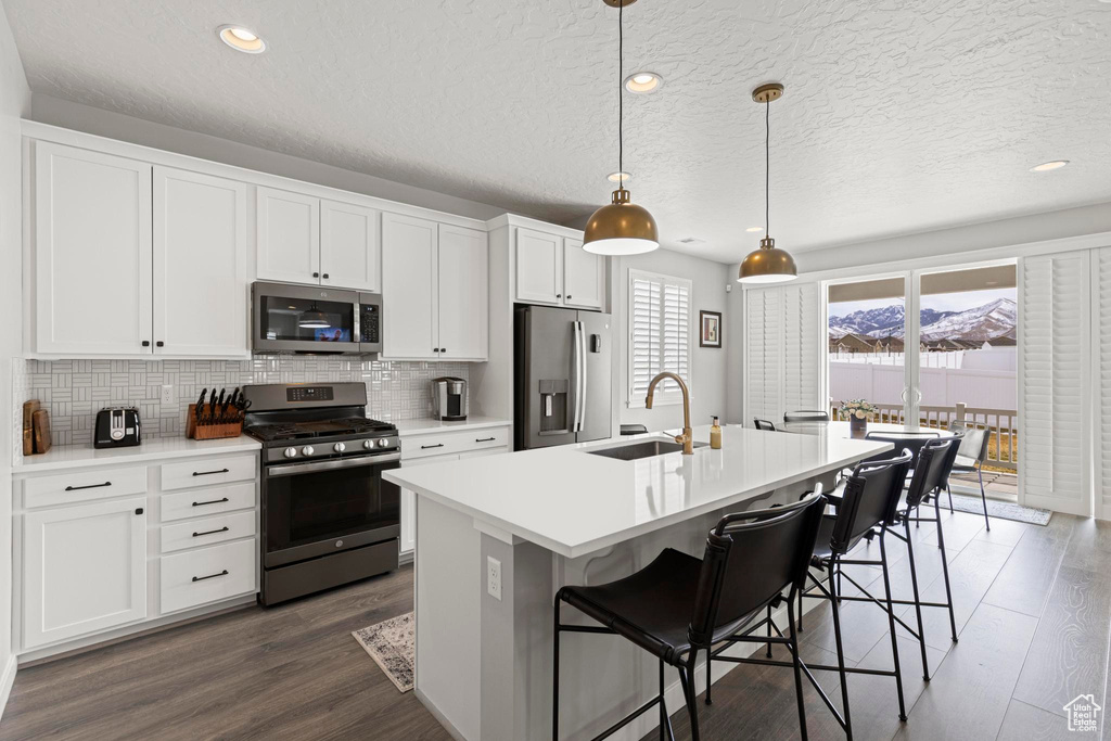 Kitchen with a sink, decorative backsplash, appliances with stainless steel finishes, and dark wood finished floors