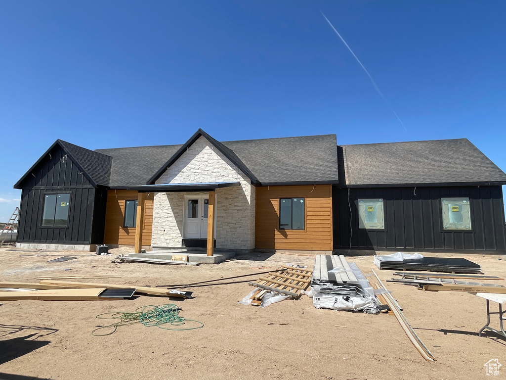 View of front of house with board and batten siding, a shingled roof, and stone siding