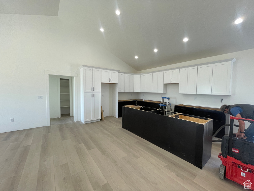 Kitchen featuring a center island, light wood-style flooring, recessed lighting, white cabinetry, and high vaulted ceiling
