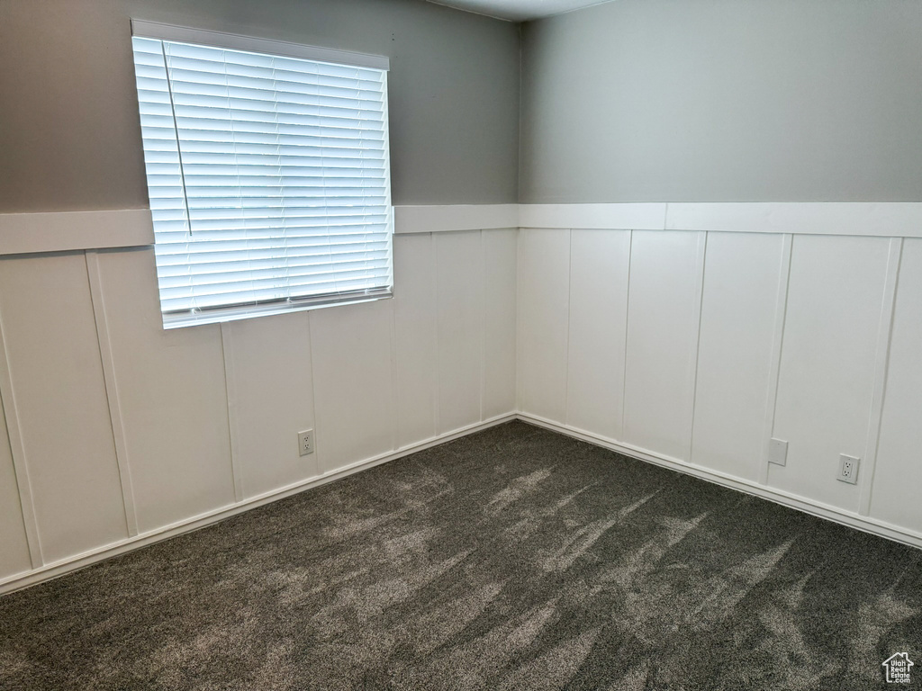 Empty room featuring a decorative wall, dark carpet, and a wainscoted wall