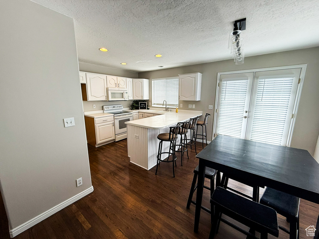 Kitchen featuring white appliances, a peninsula, a kitchen breakfast bar, baseboards, and white cabinets
