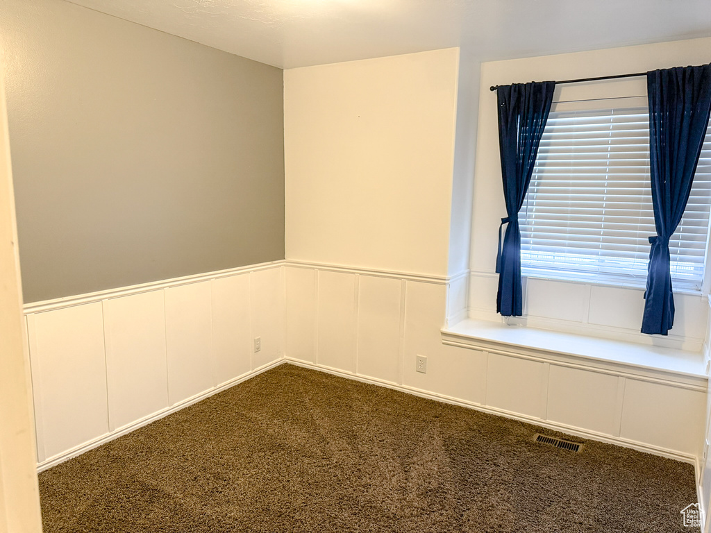 Spare room with a wainscoted wall, a decorative wall, visible vents, and dark colored carpet