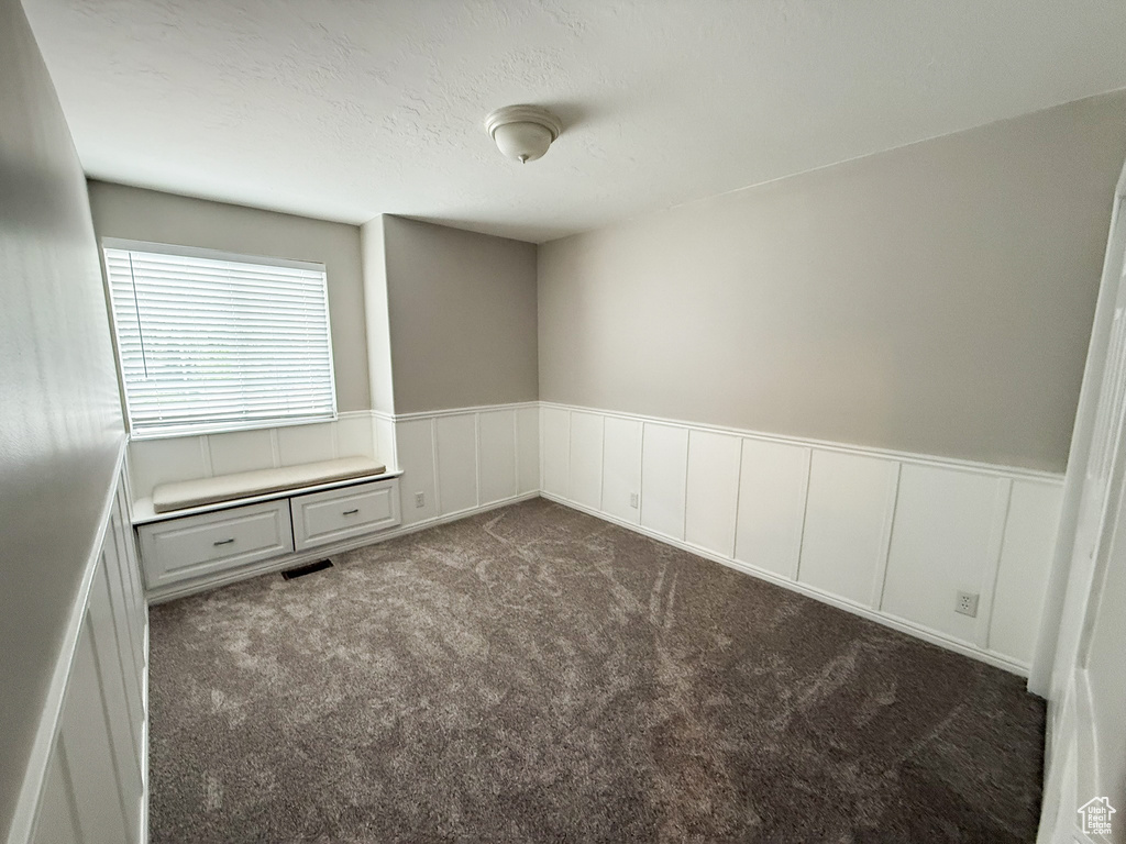 Unfurnished room featuring a wainscoted wall, carpet, and a decorative wall