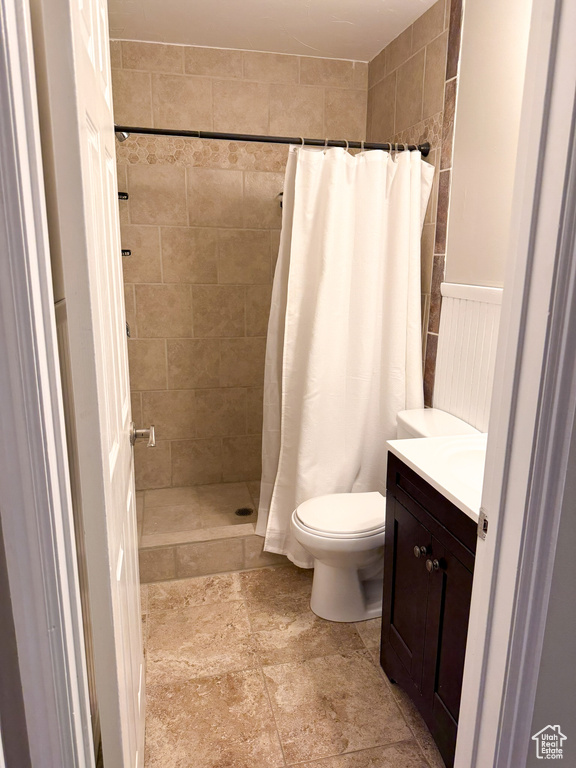 Full bathroom with tiled shower, toilet, vanity, and stone finish floors