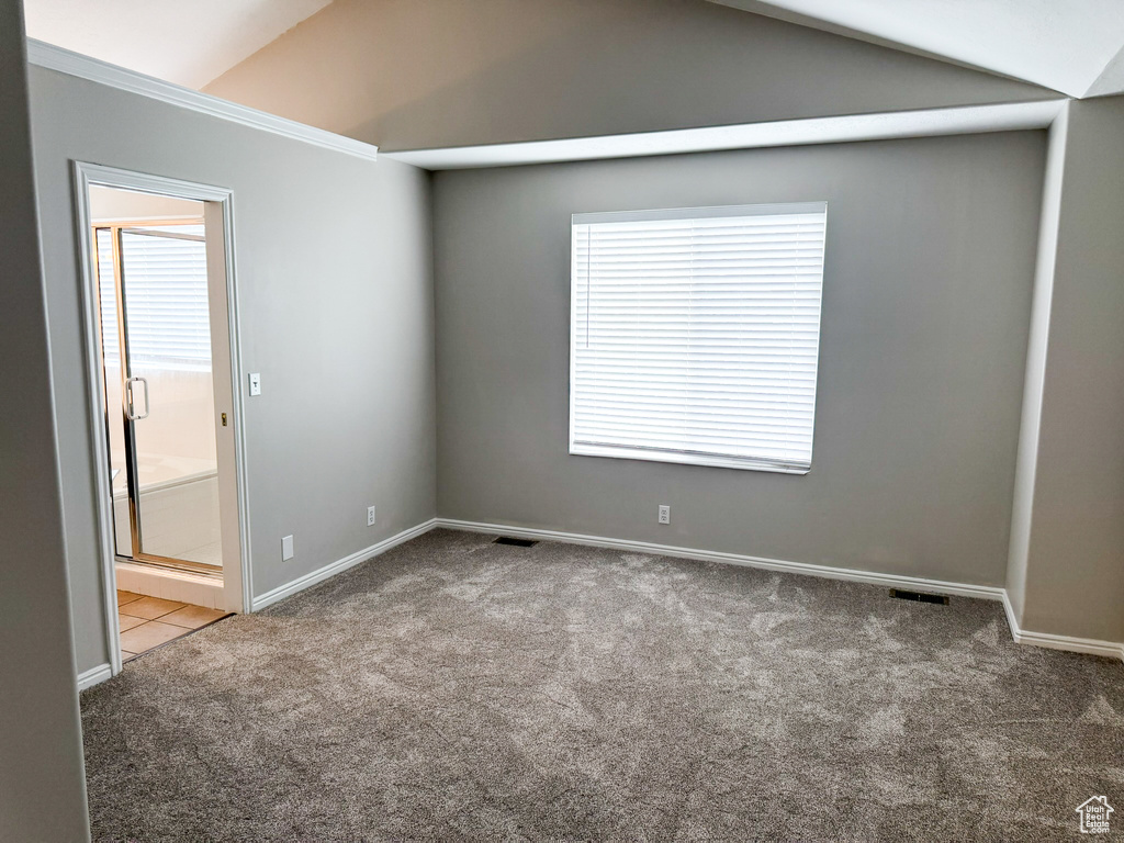 Empty room featuring carpet flooring, vaulted ceiling, and baseboards