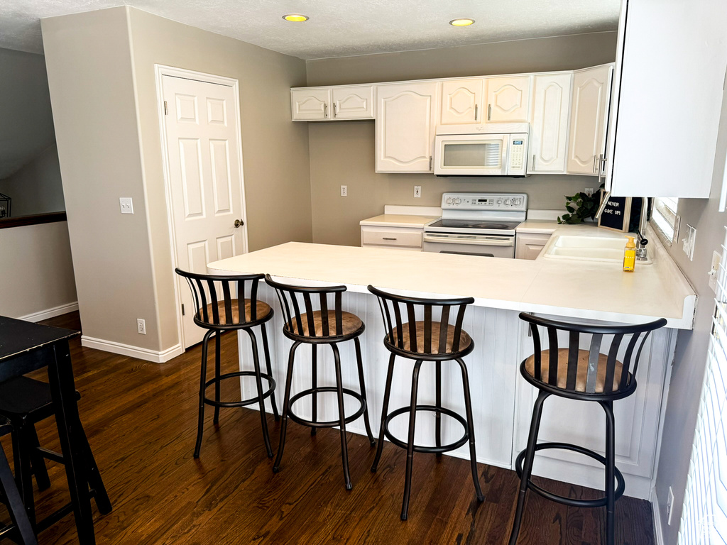 Kitchen with white appliances, a sink, dark wood-style floors, a peninsula, and white cabinetry