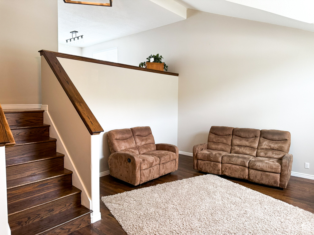 Living area featuring dark wood-type flooring, baseboards, lofted ceiling, and stairway