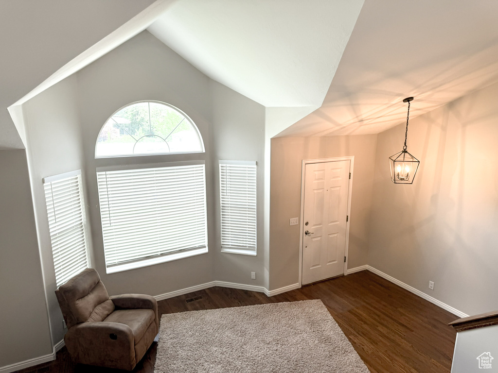 Living area featuring dark wood-style flooring, lofted ceiling, baseboards, and a chandelier