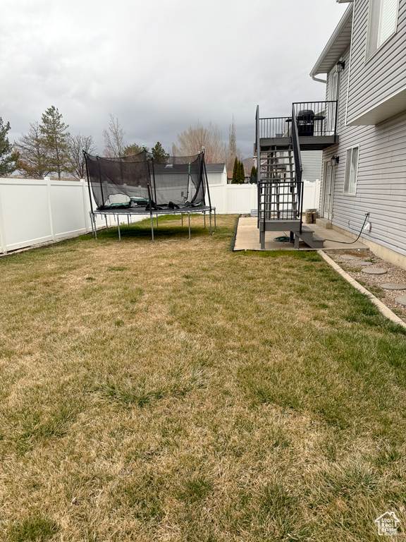 View of yard featuring a deck, stairway, a trampoline, and a fenced backyard