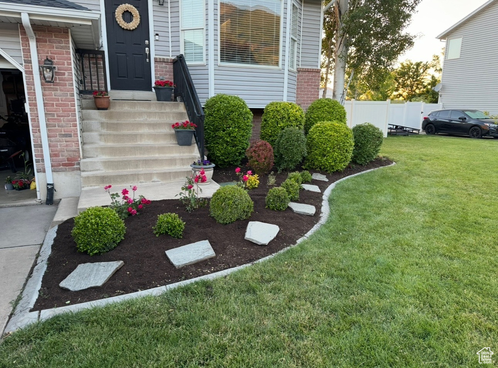 Doorway to property with a lawn, brick siding, and fence