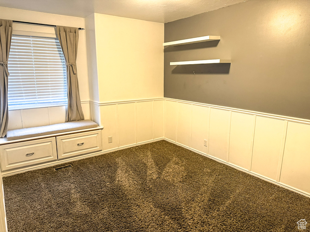 Unfurnished room featuring visible vents, a wainscoted wall, and dark carpet