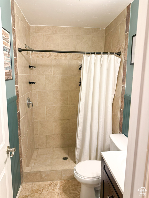 Bathroom featuring a wainscoted wall, toilet, a stall shower, and vanity