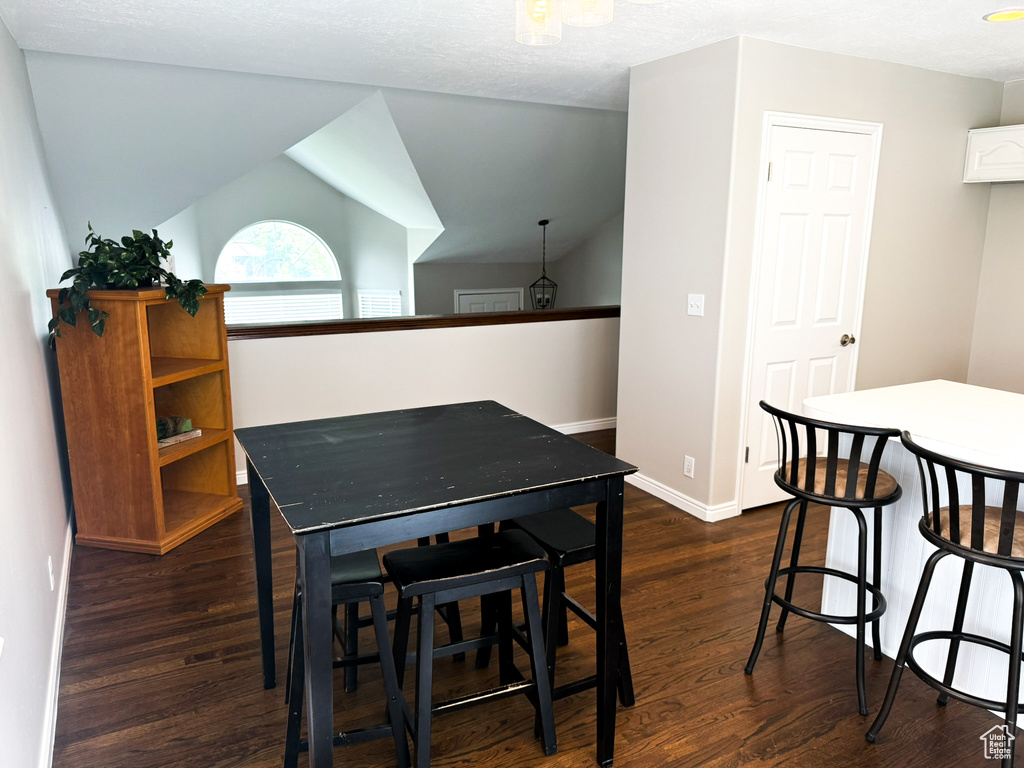 Dining space with dark wood-style flooring, baseboards, and vaulted ceiling