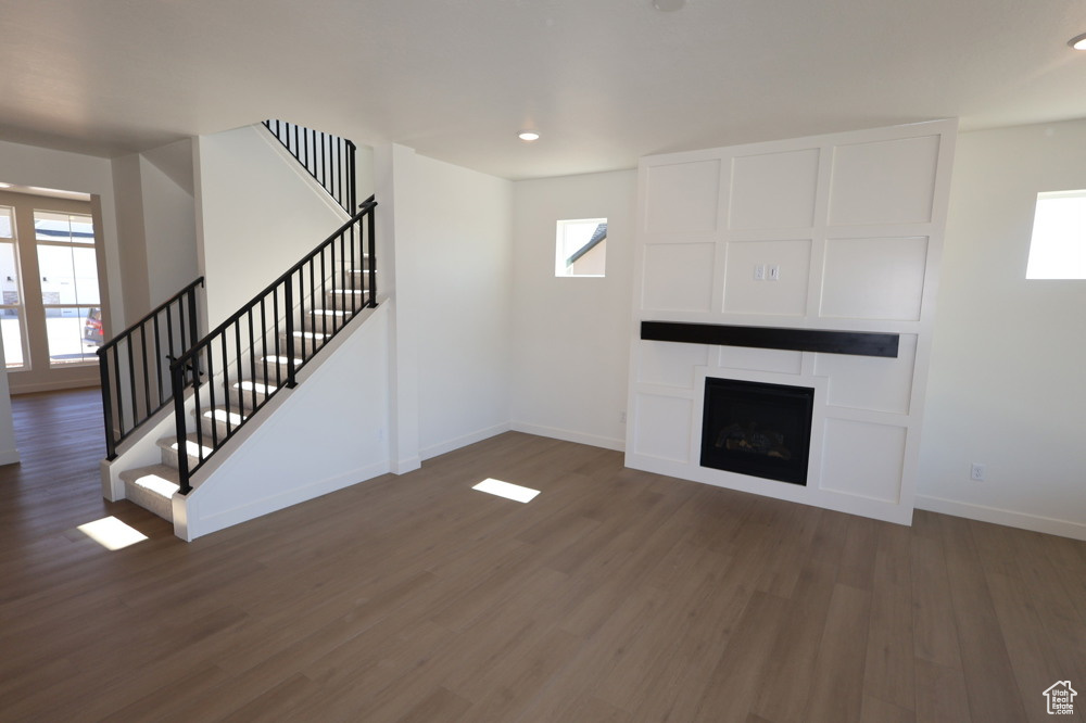 Unfurnished living room featuring baseboards, wood finished floors, stairway, and a healthy amount of sunlight