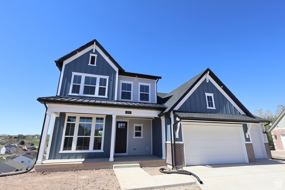 View of front of home featuring concrete driveway, a standing seam roof, board and batten siding, and covered porch