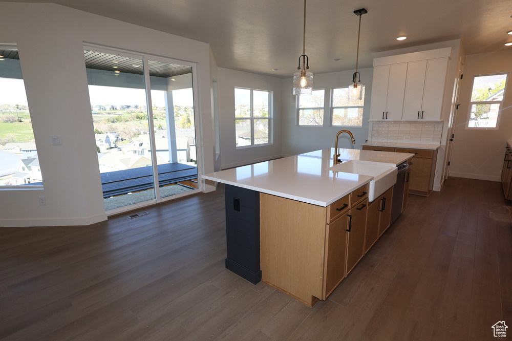 Kitchen featuring dark wood finished floors, light countertops, dishwasher, a sink, and baseboards