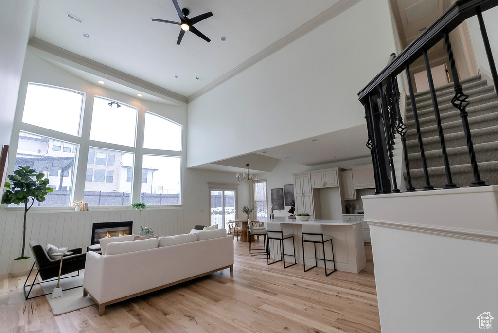Living area with light wood-style flooring, a glass covered fireplace, stairs, and ceiling fan with notable chandelier