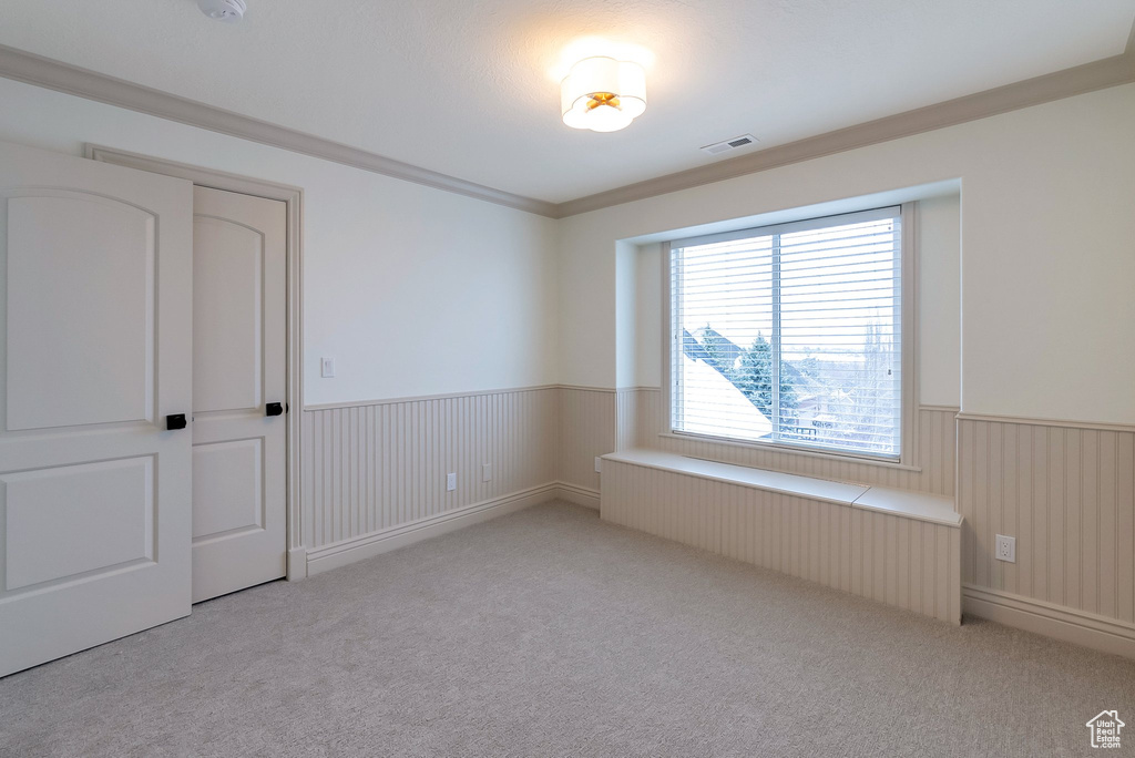 Unfurnished room featuring light carpet, radiator heating unit, visible vents, and wainscoting