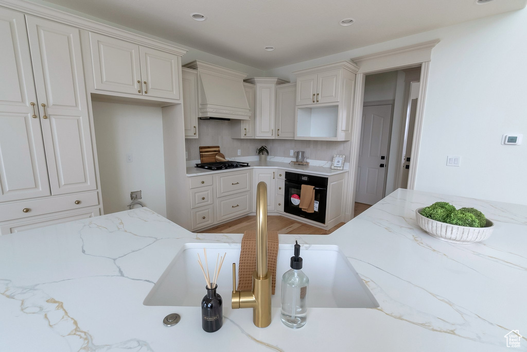 Kitchen featuring custom exhaust hood, light wood finished floors, black appliances, and light stone counters