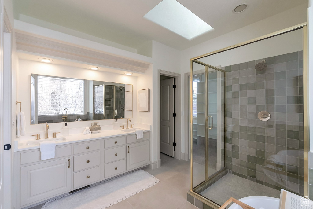 Bathroom featuring double vanity, a skylight, a stall shower, and a sink
