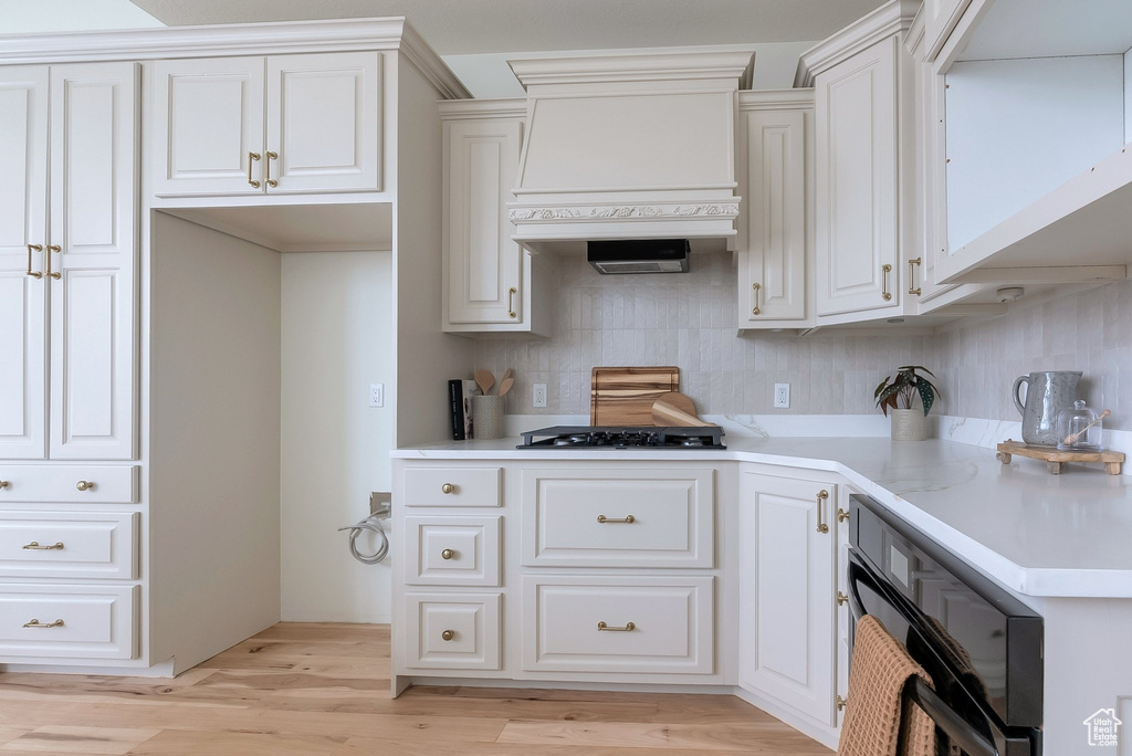 Kitchen with premium range hood, light wood-type flooring, tasteful backsplash, white cabinetry, and light countertops