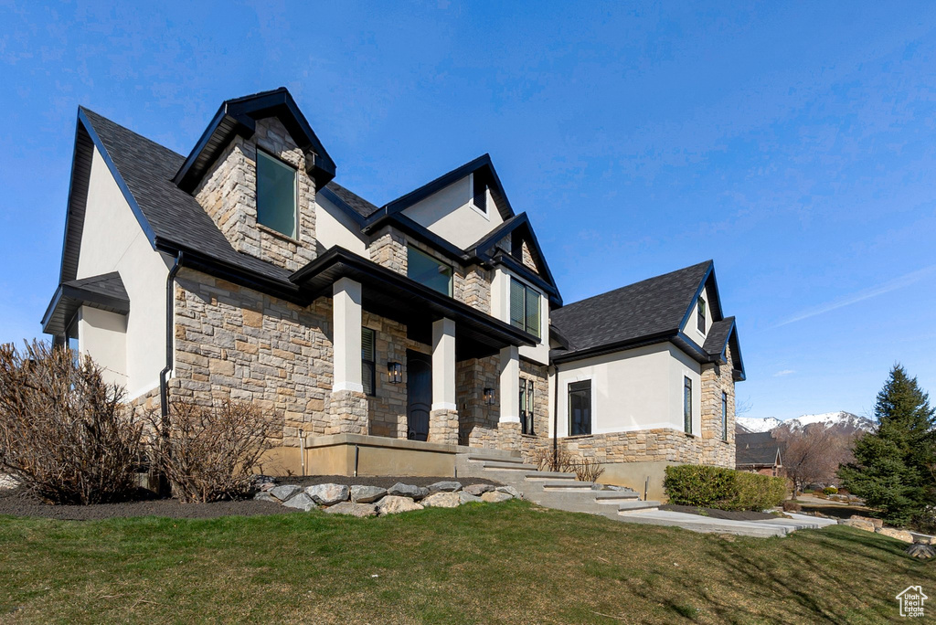 View of front facade with a front yard, stucco siding, stone siding, and a mountain view