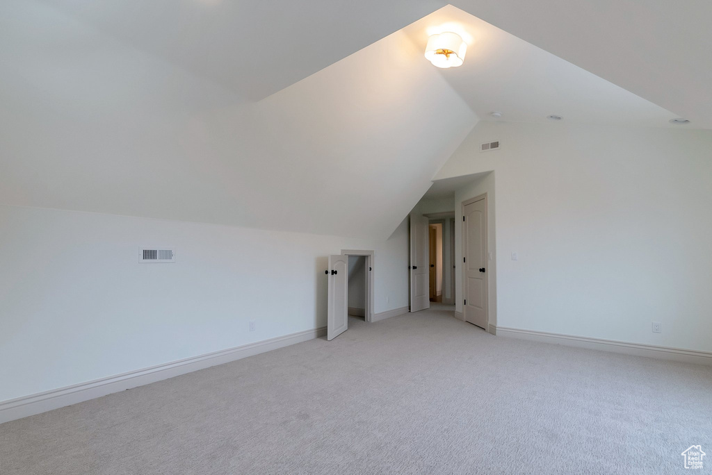 Additional living space featuring lofted ceiling, baseboards, visible vents, and light carpet