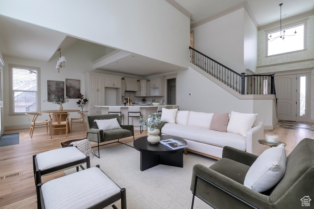 Living room featuring stairway, light wood-style floors, a towering ceiling, crown molding, and a chandelier