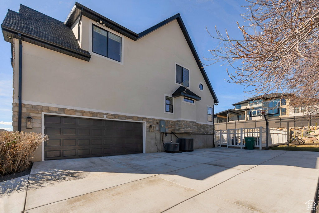 View of side of home with stone siding, driveway, fence, an attached garage, and stucco siding