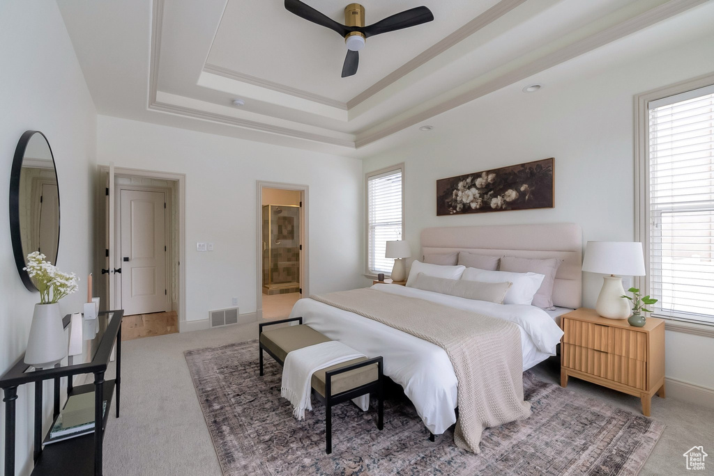Bedroom with baseboards, visible vents, ensuite bath, light carpet, and a raised ceiling