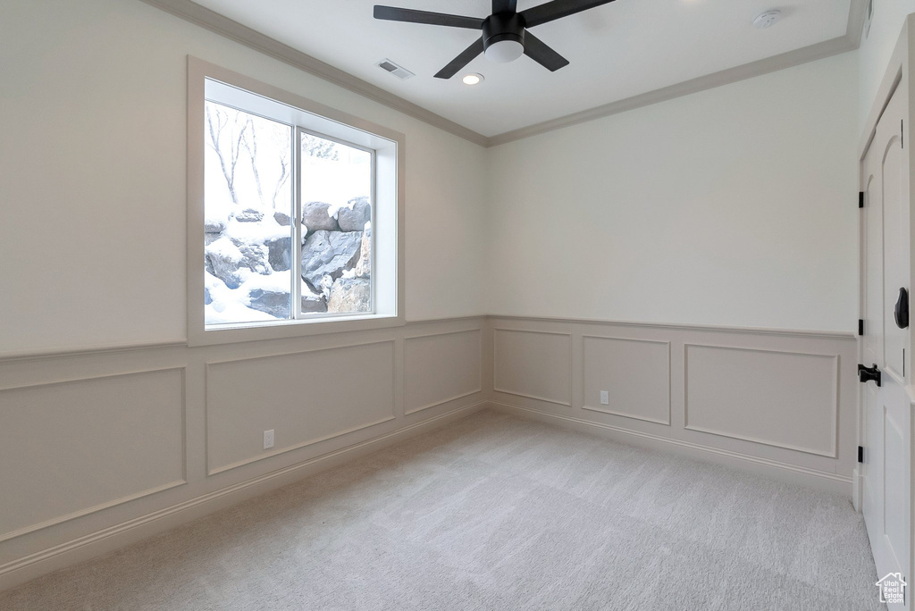 Empty room featuring visible vents, light carpet, ornamental molding, a decorative wall, and ceiling fan