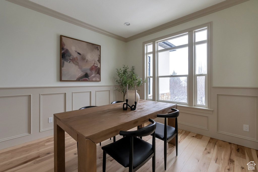Dining room featuring crown molding, a decorative wall, and light wood-style floors