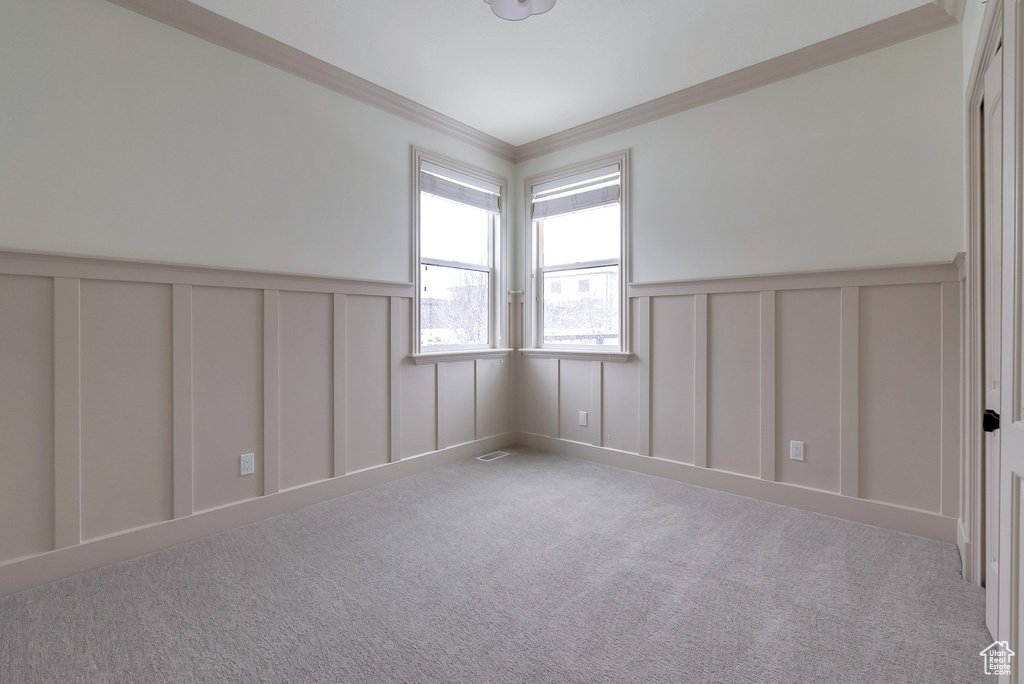 Carpeted empty room featuring a wainscoted wall, a decorative wall, visible vents, and ornamental molding
