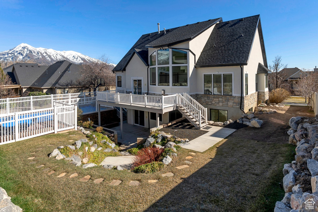Back of house with stone siding, stairway, stucco siding, fence, and a deck with mountain view