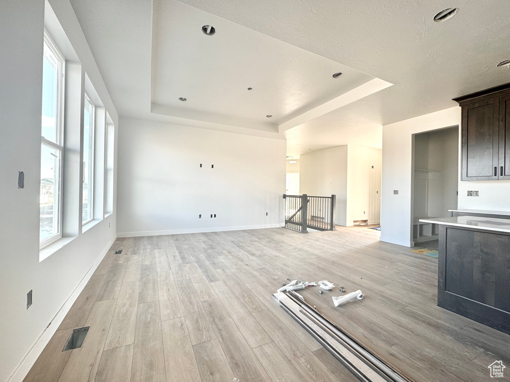 Unfurnished living room with visible vents, a raised ceiling, and light wood-style floors