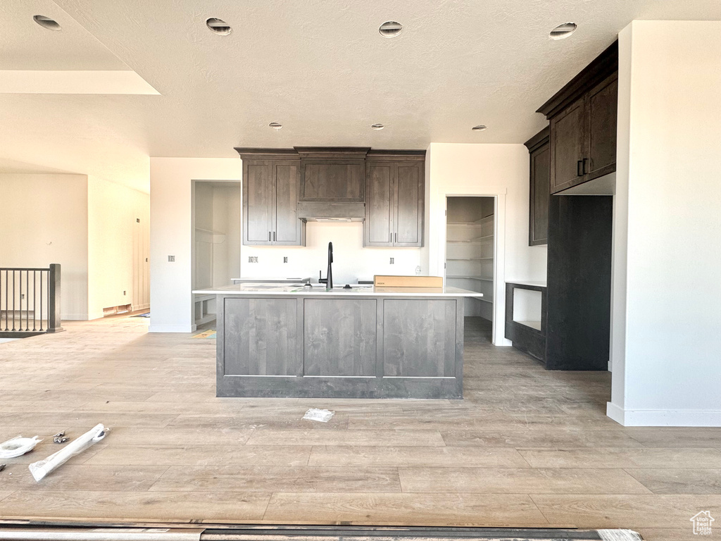 Kitchen featuring light countertops, dark brown cabinets, a center island with sink, and light wood finished floors