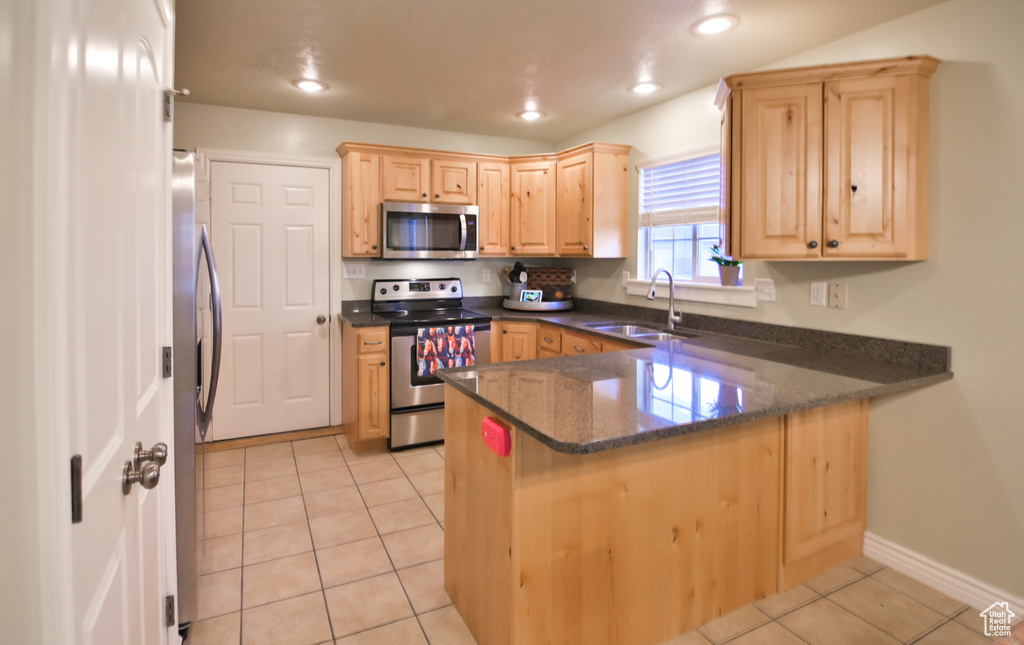 Kitchen featuring light tile patterned floors, stainless steel appliances, a peninsula, and light brown cabinetry