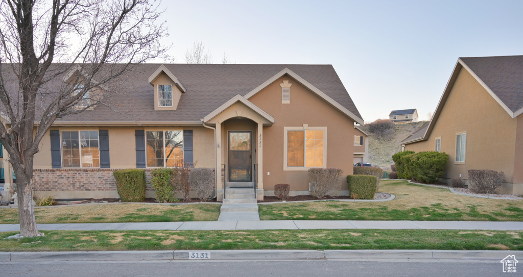 View of front facade with stucco siding, a front yard, and roof with shingles