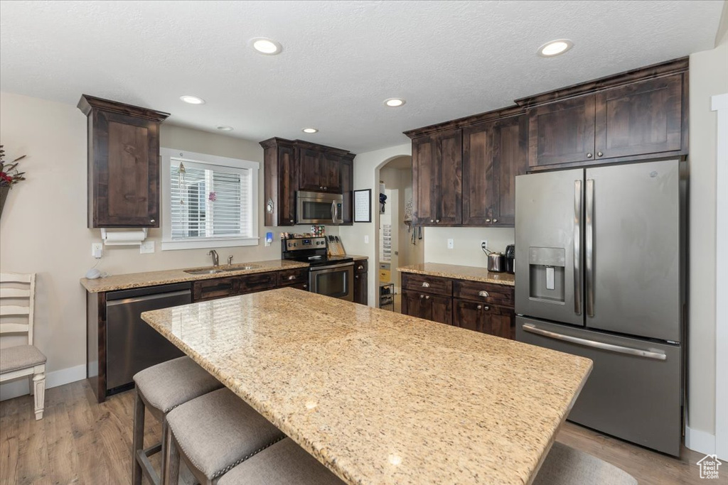 Kitchen with a breakfast bar, dark brown cabinets, appliances with stainless steel finishes, and a sink