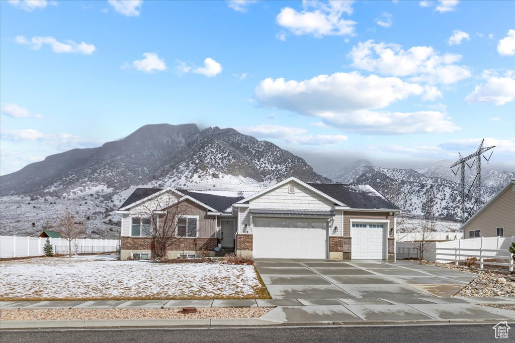 View of front facade featuring brick siding, an attached garage, fence, concrete driveway, and a mountain view