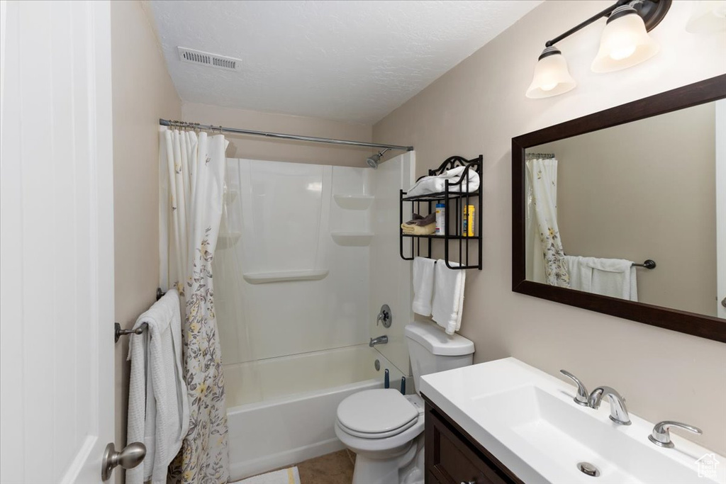 Full bathroom with visible vents, toilet, shower / bath combo, a textured ceiling, and vanity