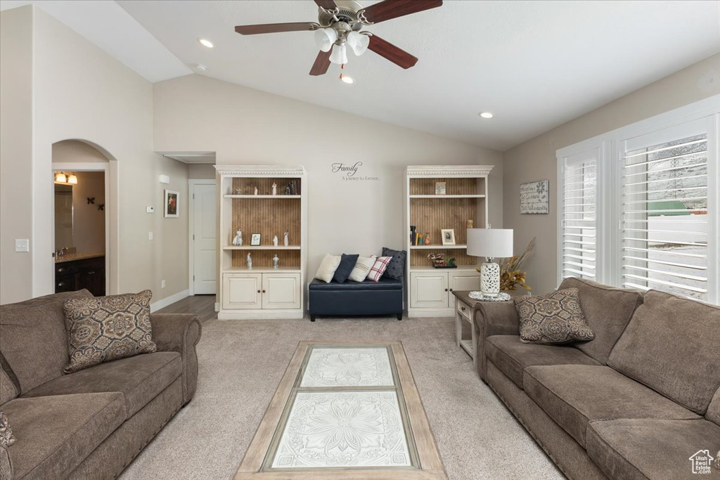 Living area with arched walkways, light colored carpet, a ceiling fan, and vaulted ceiling